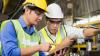 Two manufacturing workers review a factory process while holding a tablet.