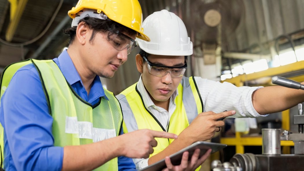 Two manufacturing workers review a factory process while holding a tablet.